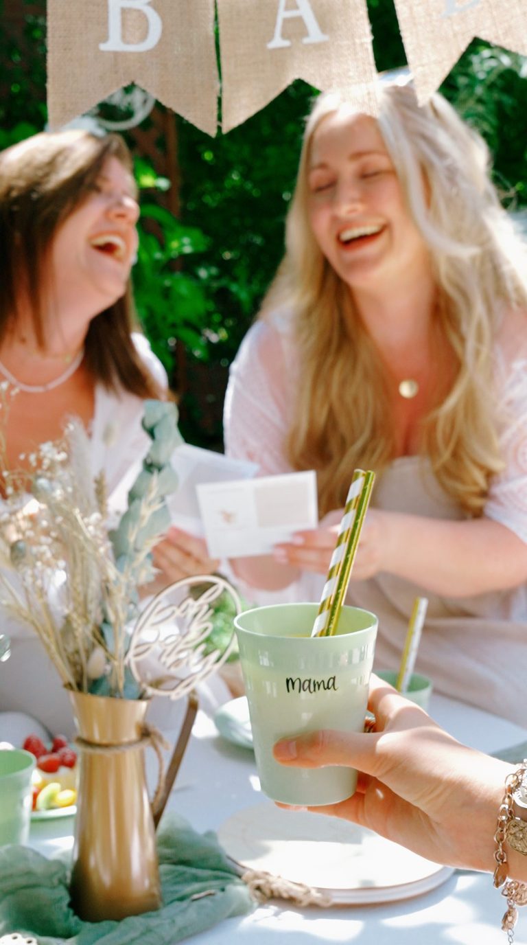 Babyshowerparty Zwei Frauen lachen bei einer Feier, Getränke und Dekorationen im Hintergrund.